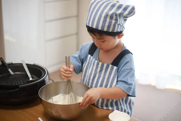 シェフの帽子をかぶったキッチンでパンケーキを作る日本人の男の子 — ストック写真