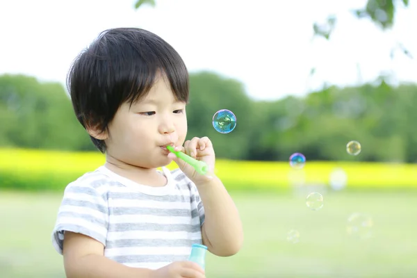 屋外の公園でシャボン玉を吹いているアジア系の少年 — ストック写真