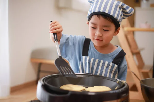 シェフの帽子をかぶったキッチンでパンケーキを作る日本人の男の子 — ストック写真