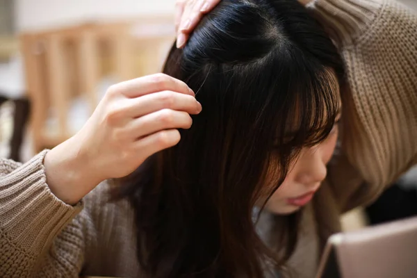 若いアジアの女性は鏡を見て 頭の上に灰色の髪を見つけようとします — ストック写真