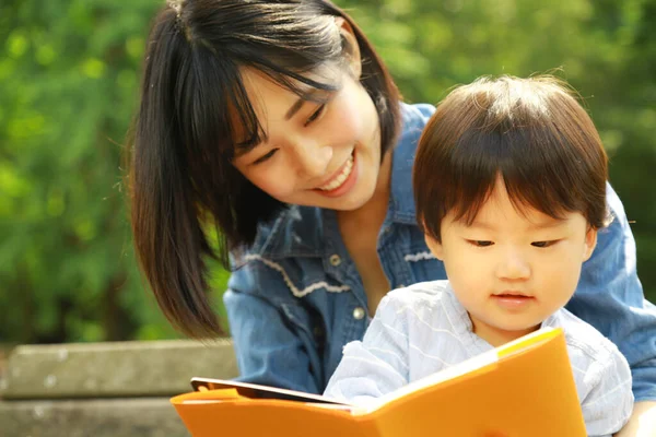 Genç Asyalı anne ve çocuğu parkta kitap okuyor.  