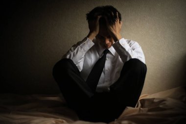 Yatakta oturan stresli Asyalı adamın portresi.