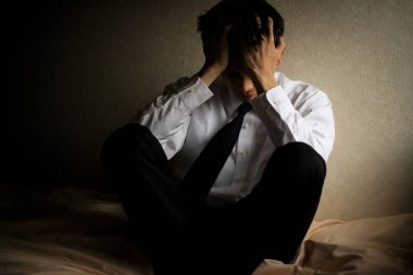 Yatakta oturan stresli Asyalı adamın portresi.