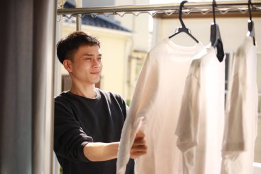 Genç Asyalı adam balkonda beyaz tişört arıyor.