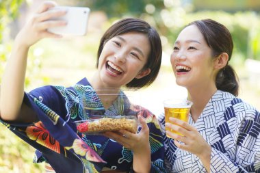 Kimonolu mutlu Asyalı kadınlar sokak yemekleriyle selfie çekiyorlar.