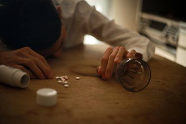 Genç adam bir sürü hap dökülmüş bir şekilde masada yatıyor. Aşırı doz uyuşturucu kavramı.