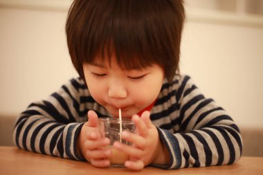 Küçük çocuk evde bardaktan içiyor.