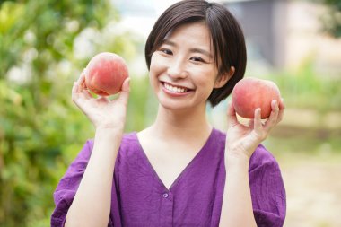 Elinde taze şeftali tutan mutlu Japon kadının portresi.