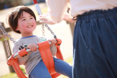Anne küçük oğlunu parkta salıncakta sallıyor.