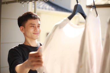 Genç Asyalı adam balkonda beyaz tişört arıyor.