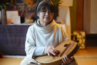 Yaşlı kadın geleneksel Japon müzik enstrümanı koto çalmak için pratik yapıyor.