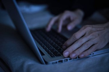 Gece geç saatlerde dizüstü bilgisayar kullanan genç adamın yakın görüntüsü.