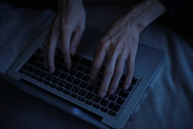 Gece geç saatlerde dizüstü bilgisayar kullanan genç adamın yakın görüntüsü.