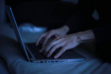 Gece geç saatlerde dizüstü bilgisayar kullanan genç adamın yakın görüntüsü.