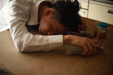 Asyalı adam alkol içecekleriyle masada yatıyor, aşırı doz konsepti. 