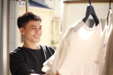 Genç Asyalı adam balkonda beyaz tişört arıyor.