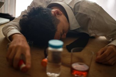 Asyalı adam alkol içecekleriyle masada yatıyor, aşırı doz konsepti. 