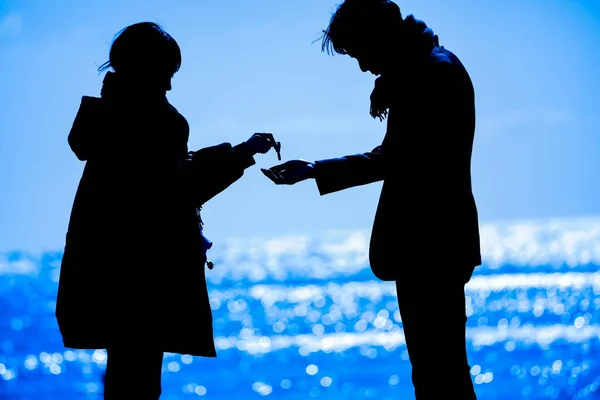 Silhouetten Van Vrouw Geven Sleutels Aan Jonge Man Aan Zeekust — Stockfoto