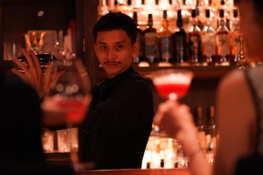 Yakışıklı Asyalı barmen barda içki yapıyor.