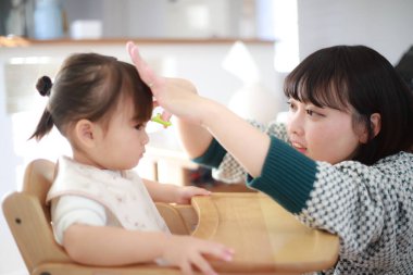 Genç Japon anne küçük kızı için saç kesiyor. 