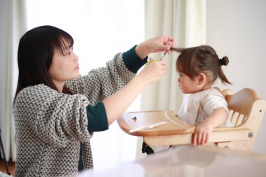 Genç Japon anne küçük kızı için saç kesiyor. 