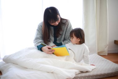 Güzel genç anne, küçük kızıyla yatakta kitap okuyor.
