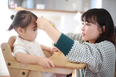 Genç Japon anne küçük kızı için saç kesiyor. 