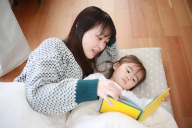 Güzel genç anne, küçük kızıyla yatakta kitap okuyor.