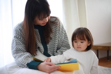 Güzel genç anne, küçük kızıyla yatakta kitap okuyor.