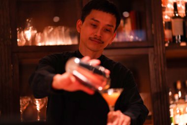 Yakışıklı Asyalı barmen barda içki yapıyor.