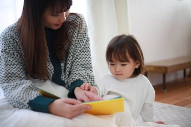Güzel genç anne, küçük kızıyla yatakta kitap okuyor.
