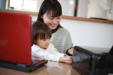 Küçük kızıyla evden çalışan Asyalı genç bir kadın.