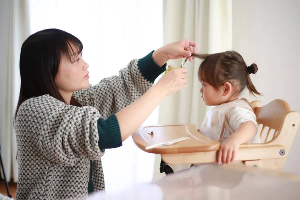 Genç Japon anne küçük kızı için saç kesiyor. 