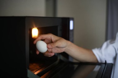 Mikrodalgada yumurta ısıtmaya çalışan bir adam.