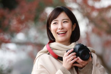 Açık havada fotoğraf çeken gülümseyen Asyalı bir kadın. 