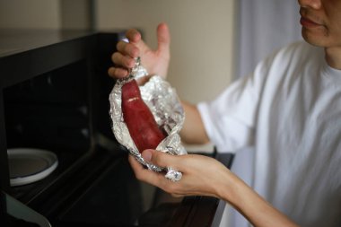 Patatesleri alüminyum folyoya sarıp mikrodalgada ısıtmaya çalışan bir adam.