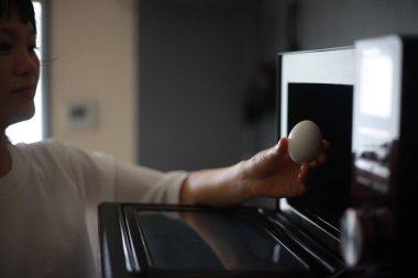 Bir kadın mikrodalgada yumurta ısıtmaya çalışıyor.