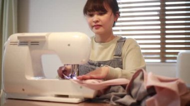 Güzel genç bir kadın dikiş makinesine dikiş dikiyor.