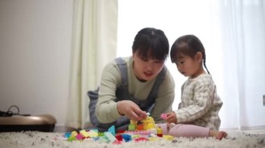 Anne, küçük kızıyla evde yerde oynuyor.