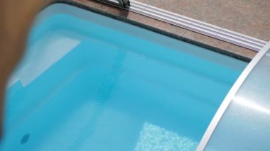 Odadaki pencerenin üzerindeki kahverengi perde hafif esintide esiyordu. Dışarıda bir yüzme havuzu var. Güneşli hava.