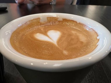 Koyu seramik fincanda kalbi olan bir kahve.