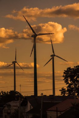 Gün batımında rüzgar türbini jeneratörlerinin siluetleri köyü besliyor. Alternatif yenilenebilir enerji üretimi
