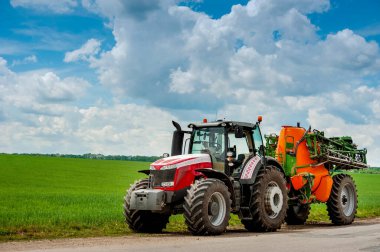 Turuncu spreyli kırmızı traktör yolda gidiyor, bahar gübresi, güzel gökyüzü.