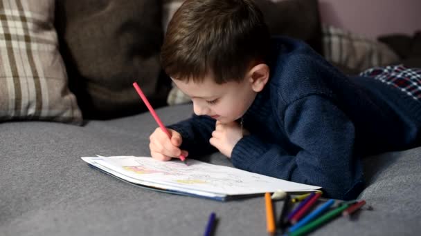 hezký chlapec kreslí s barevnými tužkami v omalovánky ležící. Kreativita a šťastné dětství