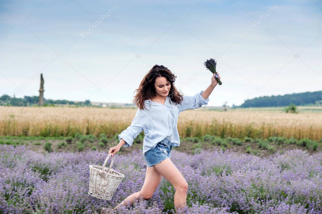 happy girl runs in a lavender field, holding a basket and a bouquet of flowers