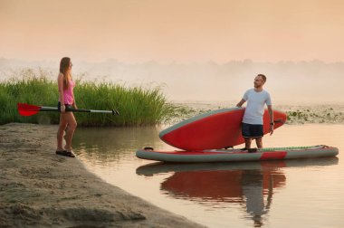 a girl and a boy are preparing to swim on a stand-up paddle board, active recreation of lovers, tourism on the water