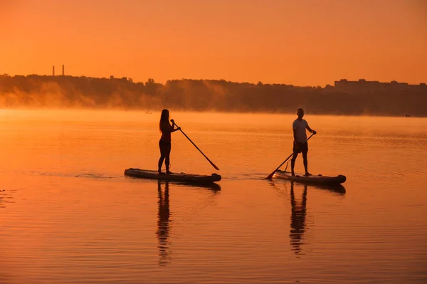 Silhouettes Couple Sup Boards Water Lake Background Red Sky Morning — Stock Fotó