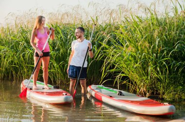 a young couple walks along the river on a paddle board, interesting communication.