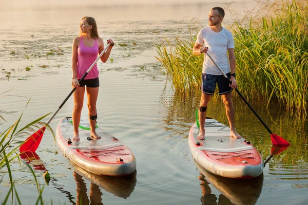a young couple walks along the river on a paddle board., morning light