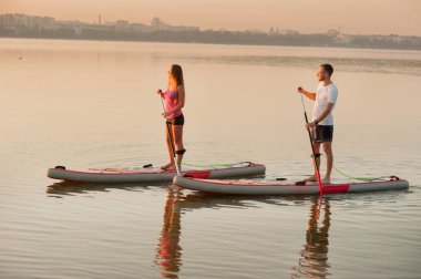 a young couple walks along the river on a on an inflatable SUP board , double skating